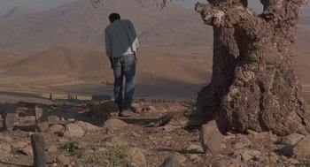 Movie still from “The Wind Will Carry Us” (1999), directed by Abbas Kiarostami – A man standing on top of a hill next to a tree; Extreme Wide shot, Low angle