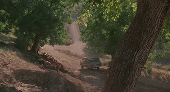 Movie still from “The Wind Will Carry Us” (1999), directed by Abbas Kiarostami – A truck driving down a dirt road near trees; Extreme Wide shot, High angle