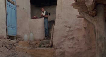 Movie still from “The Wind Will Carry Us” (1999), directed by Abbas Kiarostami – A man standing in a doorway of an old building; Wide shot, Low angle
