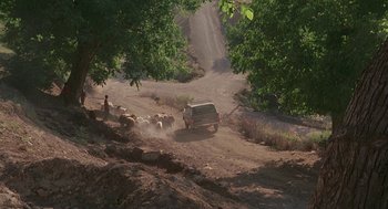 Movie still from “The Wind Will Carry Us” (1999), directed by Abbas Kiarostami – A truck driving down a dirt road with a herd of sheep in the background; Extreme Wide shot, High angle
