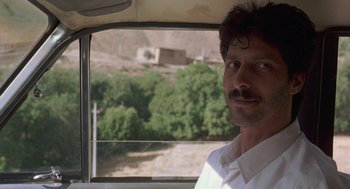 Movie still from “The Wind Will Carry Us” (1999), directed by Abbas Kiarostami – A man standing in the driver's seat of a car; Close Up shot, Low angle