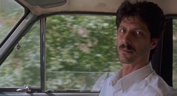 Movie still from “The Wind Will Carry Us” (1999), directed by Abbas Kiarostami – A man sitting in the driver's seat of a car; Close Up shot, Low angle