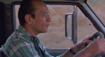 Movie still from “The Wind Will Carry Us” (1999), directed by Abbas Kiarostami – A man driving a car in the desert; Close Up shot, Low angle