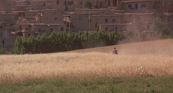 Movie still from “The Wind Will Carry Us” (1999), directed by Abbas Kiarostami – A man riding a bike through a field of grass; Extreme Wide shot, High angle