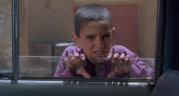Movie still from “The Wind Will Carry Us” (1999), directed by Abbas Kiarostami – A young boy in a purple shirt is looking at the camera; Close Up shot, Low angle