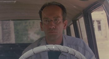 Movie still from “The Wind Will Carry Us” (1999), directed by Abbas Kiarostami – A man with glasses is driving a car; Close Up shot, Low angle