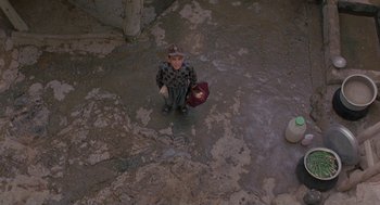Movie still from “The Wind Will Carry Us” (1999), directed by Abbas Kiarostami – A little boy is holding a hat and a bag in his hands; Wide shot, Overhead angle