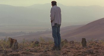 Movie still from “The Wind Will Carry Us” (1999), directed by Abbas Kiarostami – A man standing on top of a hill looking out at a valley; Extreme Wide shot, Low angle
