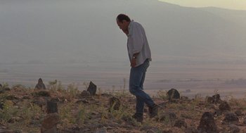 Movie still from “The Wind Will Carry Us” (1999), directed by Abbas Kiarostami – A man standing on top of a dirt hill; Wide shot, Low angle