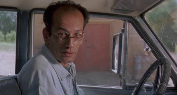 Movie still from “The Wind Will Carry Us” (1999), directed by Abbas Kiarostami – A man with glasses sitting in the driver's seat of a car; Close Up shot, Low angle