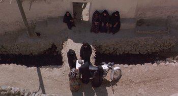 Movie still from “The Wind Will Carry Us” (1999), directed by Abbas Kiarostami – A group of women sitting around a motorcycle; Wide shot, Overhead angle