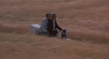 Movie still from “The Wind Will Carry Us” (1999), directed by Abbas Kiarostami – Two men sitting on a bike in the middle of a field; Wide shot, Low angle