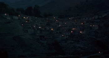 Movie still from “The Wind Will Carry Us” (1999), directed by Abbas Kiarostami – A large group of houses on top of a hill at night; Extreme Wide shot, High angle