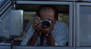 Movie still from “The Wind Will Carry Us” (1999), directed by Abbas Kiarostami – A man taking a picture through a car window; Close Up shot, Low angle