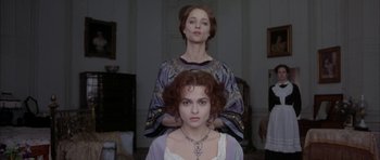 Movie still from “The Wings of the Dove” (1997), directed by Iain Softley – A woman sitting on top of another woman's head in a room; Medium shot, Low angle