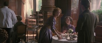 Movie still from “The Wings of the Dove” (1997), directed by Iain Softley – Two women are standing at a table with a cake; Wide shot, High angle