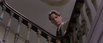 Movie still from “The Wings of the Dove” (1997), directed by Iain Softley – A man standing on top of a wooden stair case railing; Close Up shot, Low angle