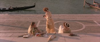 Movie still from “The Wings of the Dove” (1997), directed by Iain Softley – Three people sitting at a table near a body of water; Wide shot, High angle