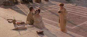 Movie still from “The Wings of the Dove” (1997), directed by Iain Softley – Two women and a man sitting on the side of the street; Wide shot, High angle