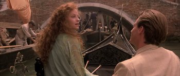 Movie still from “The Wings of the Dove” (1997), directed by Iain Softley – A woman sitting in front of a boat with people in the background; Medium shot, Over the shoulder angle