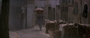 Movie still from “The Wings of the Dove” (1997), directed by Iain Softley – A person with an umbrella walking down a street; Wide shot, Low angle