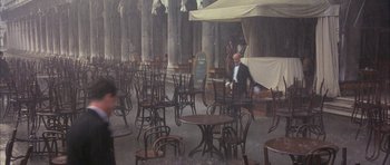 Movie still from “The Wings of the Dove” (1997), directed by Iain Softley – A man in a suit and tie sitting at an outdoor cafe; Wide shot, High angle