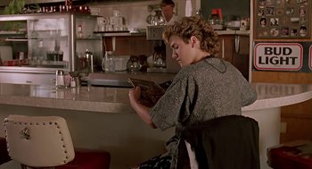 Movie still from “The Wizard” (1989), directed by Todd Holland – A woman sitting at a counter reading a magazine; Medium shot, Over the shoulder angle