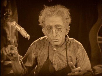 Movie still from “The Wizard of Oz” (1925), directed by Larry Semon – An old man wearing glasses is sitting in a chair; Medium shot, High angle