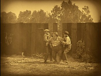 Movie still from “The Wizard of Oz” (1925), directed by Larry Semon – A group of men standing next to each other on top of a dirt field; Wide shot, High angle