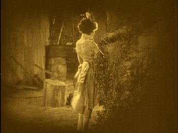 Movie still from “The Wizard of Oz” (1925), directed by Larry Semon – An old photo of a woman standing in front of a tree; Wide shot, High angle