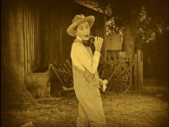Movie still from “The Wizard of Oz” (1925), directed by Larry Semon – An old photo of a man smoking a cigarette outside; Wide shot, High angle