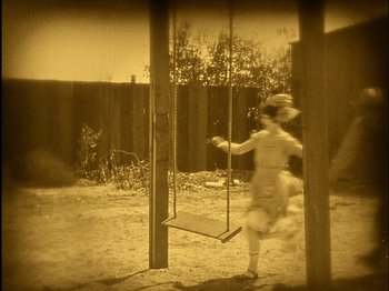 Movie still from “The Wizard of Oz” (1925), directed by Larry Semon – An old photo of a child swinging on a swing set; Wide shot, High angle