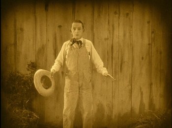 Movie still from “The Wizard of Oz” (1925), directed by Larry Semon – An old photo of a man holding a cowboy hat; Medium shot, High angle