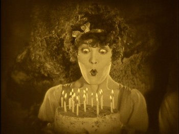 Movie still from “The Wizard of Oz” (1925), directed by Larry Semon – An old photo of a woman blowing out the candles on a cake; Extreme Close Up shot, Overhead angle