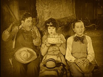 Movie still from “The Wizard of Oz” (1925), directed by Larry Semon – A group of people that are sitting around a cake; Medium shot, High angle