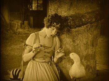Movie still from “The Wizard of Oz” (1925), directed by Larry Semon – An old photo of a woman standing next to a bird; Medium shot, High angle