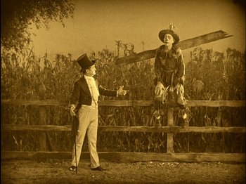 Movie still from “The Wizard of Oz” (1925), directed by Larry Semon – An old photo of a man and a woman standing next to each other; Wide shot, High angle