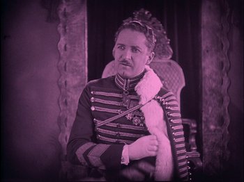 Movie still from “The Wizard of Oz” (1925), directed by Larry Semon – A man dressed in a military uniform sitting in a chair; Medium shot, High angle