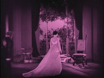 Movie still from “The Wizard of Oz” (1925), directed by Larry Semon – A woman in a white dress standing in front of a window; Wide shot, High angle