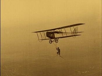 Movie still from “The Wizard of Oz” (1925), directed by Larry Semon – An old airplane flying through the air with a person hanging from it; Wide shot, Low angle