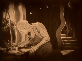 Movie still from “The Wizard of Oz” (1925), directed by Larry Semon – An old man is working on something on a table; Medium shot, High angle