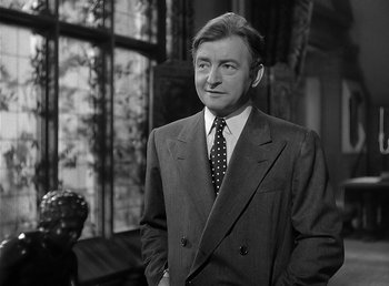 Movie still from “The Wolf Man” (1941), directed by George Waggner – A man in a suit and tie standing in front of a window; Medium shot, Over the shoulder angle