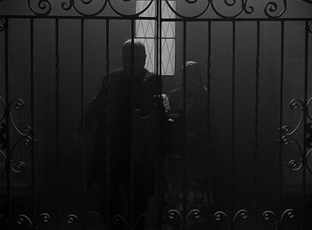 Movie still from “The Wolf Man” (1941), directed by George Waggner – A person standing behind a gate in the dark; Wide shot, Low angle