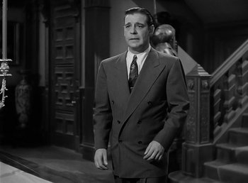 Movie still from “The Wolf Man” (1941), directed by George Waggner – A man in a suit and tie standing next to a staircase; Medium shot, Low angle