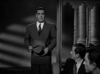 Movie still from “The Wolf Man” (1941), directed by George Waggner – A black and white photo of a man holding a hat; Medium shot, Over the shoulder angle