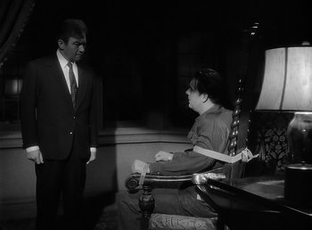 Movie still from “The Wolf Man” (1941), directed by George Waggner – A man in a suit and tie standing next to a woman in a chair; Medium shot, Over the shoulder angle
