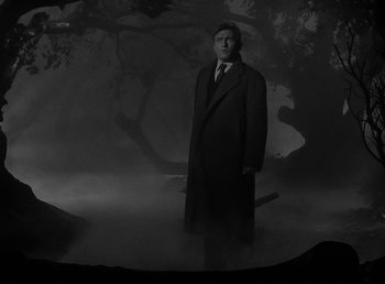 Movie still from “The Wolf Man” (1941), directed by George Waggner – A man in a suit and tie standing in the fog in front of a tree; Wide shot, Low angle