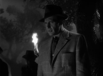 Movie still from “The Wolf Man” (1941), directed by George Waggner – A man in a suit and hat holding a lit match; Close Up shot, Over the shoulder angle
