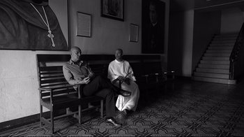 Two men sitting on a wooden bench in a room