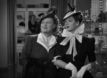 Movie still from “The Women” (1939), directed by George Cukor – Two women in hats and gloves standing next to each other; Medium shot, Low angle
